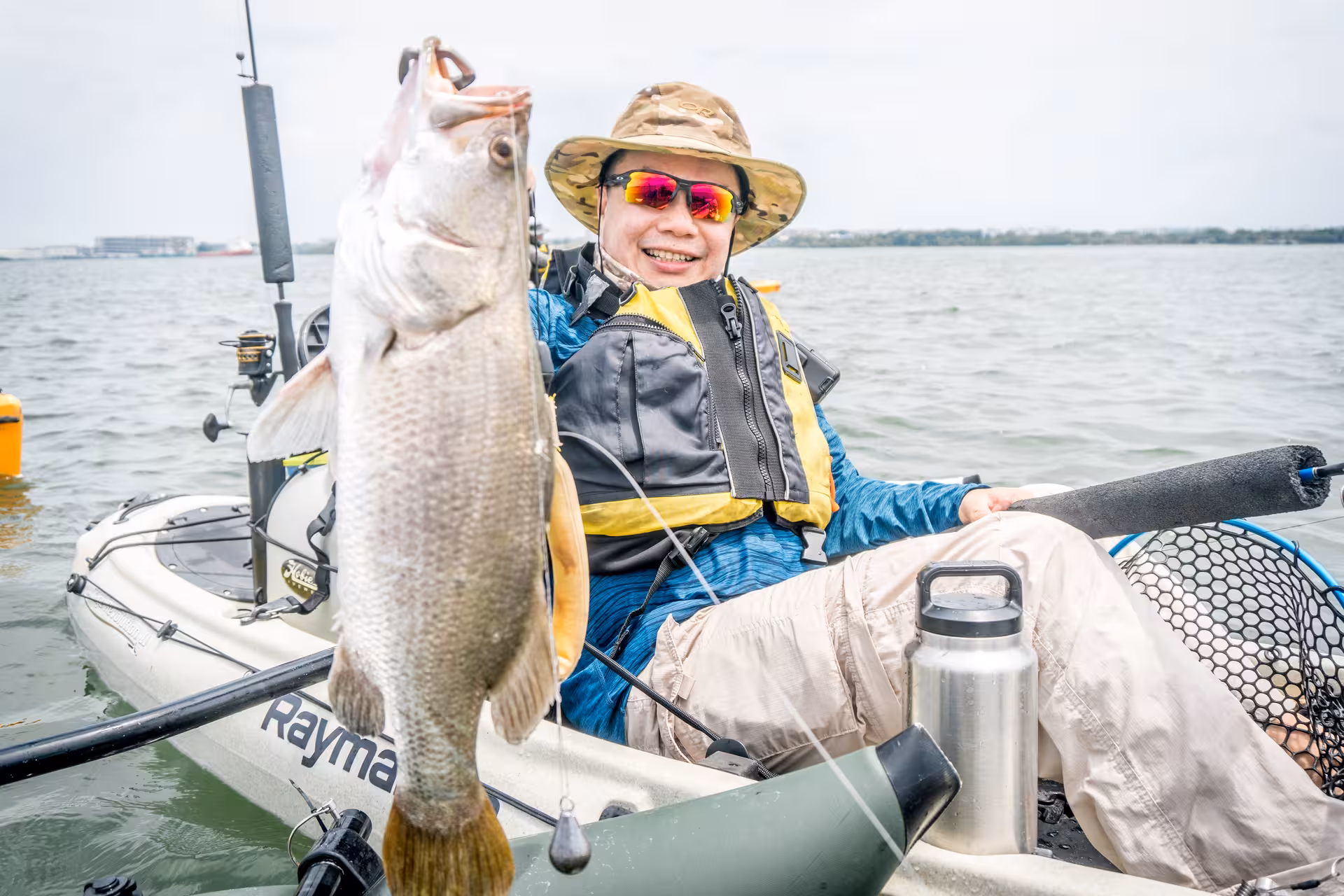 Smiling kayaker holds a large fish caught during kayak fishing tour at Pulau Ubin mangroves.
