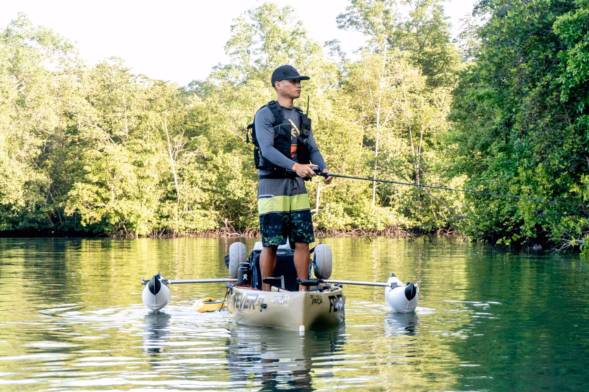Fisherman stands poised on kayak, casting line in serene Pulau Ubin mangrove waters.