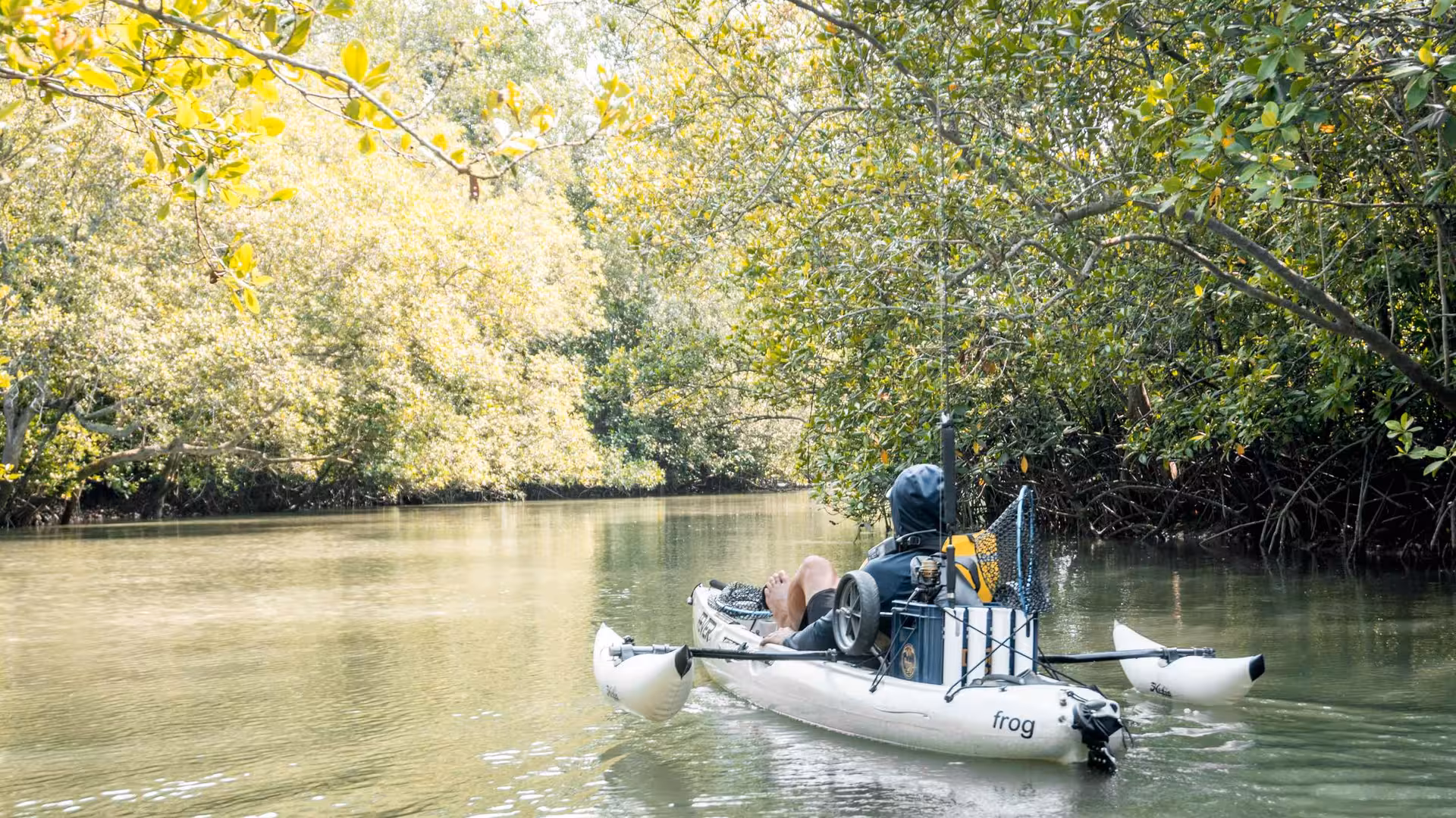 Solo kayaker navigates tranquil waters of Pulau Ubin mangroves, surrounded by vibrant greenery and sunshine.