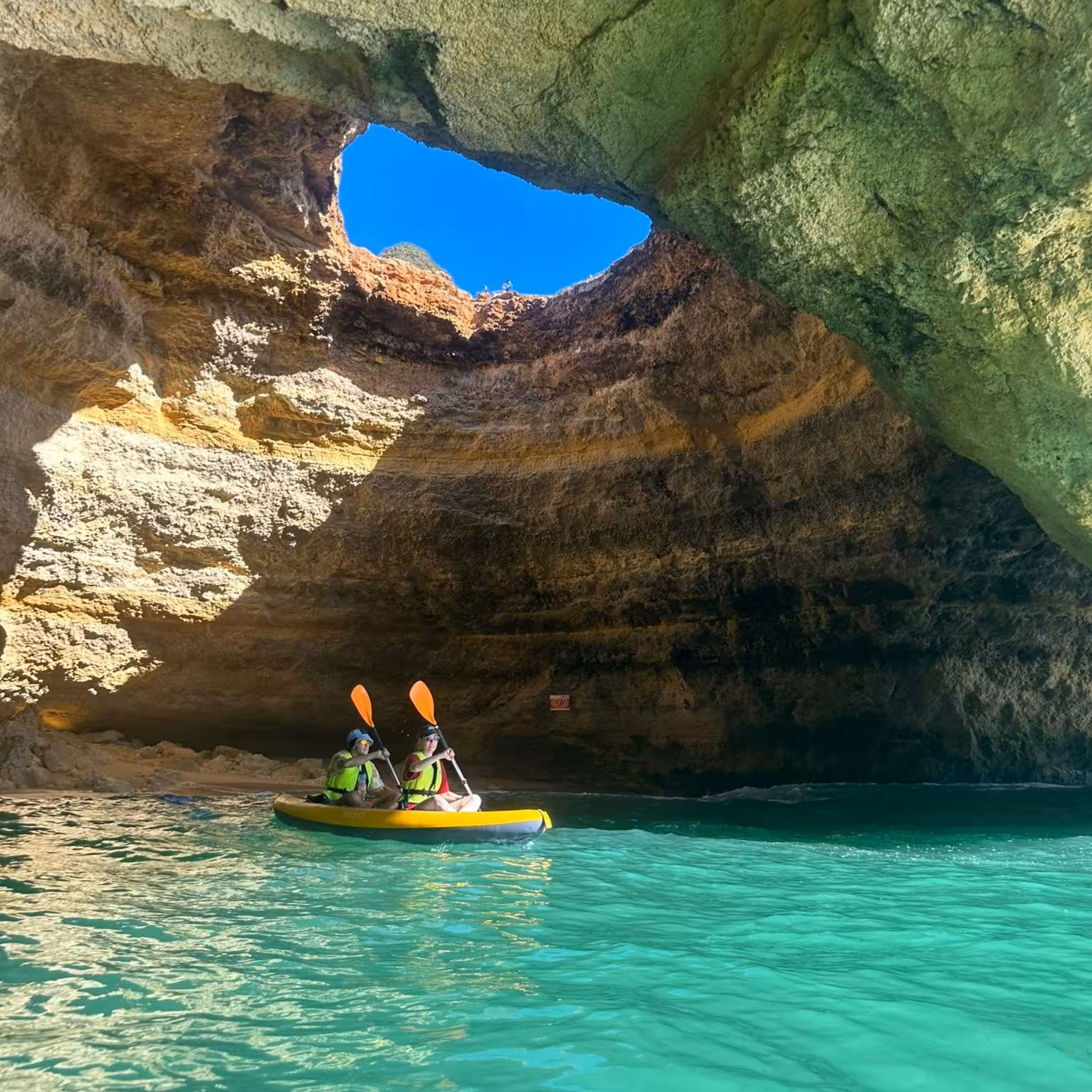 Kayakers exploring a stunning sea cave with turquoise waters on a guided adventure tour.