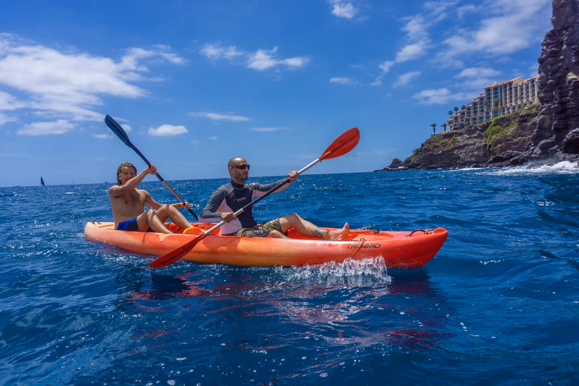 Two people kayaking on clear blue waters near a rocky coastline, enjoying a guided tour with snorkeling options.
