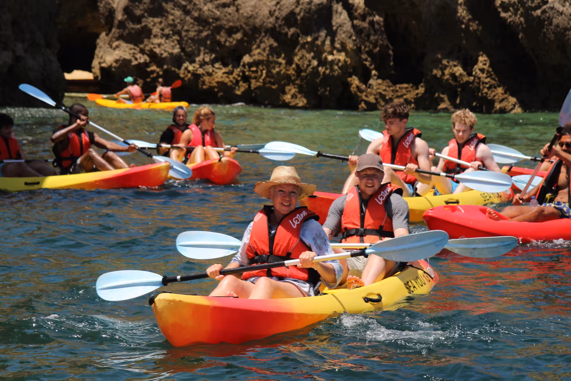 Group kayak tour in Lagos, Portugal with happy travelers paddling colorful tandem kayaks along dramatic rocky coastline