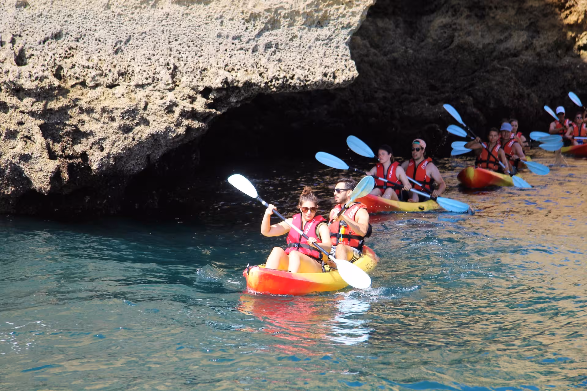 Group kayaking tour in Lagos, Portugal paddling past dramatic sea caves and cliffs on clear turquoise Atlantic water
