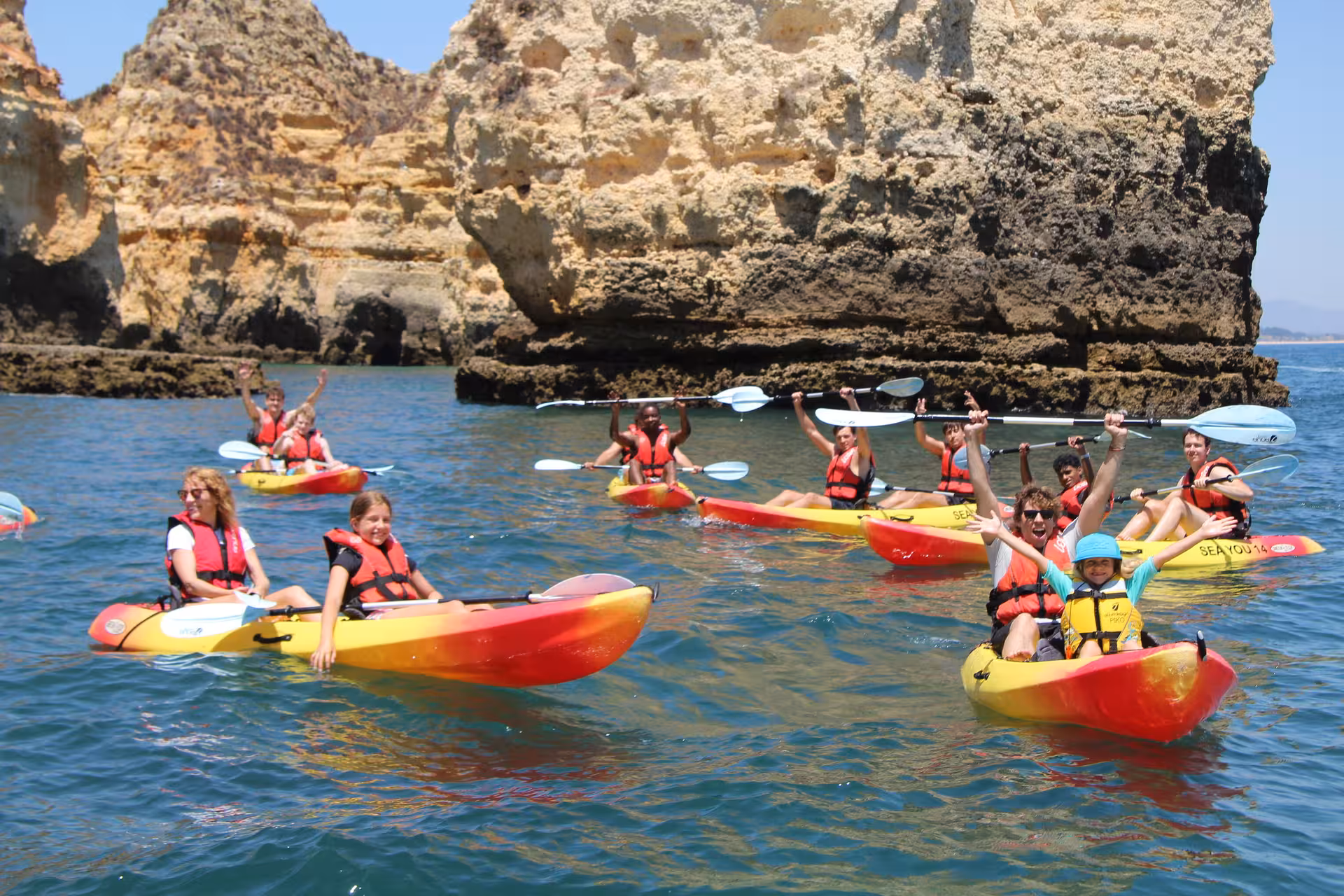 Smiling kayakers paddle along dramatic golden cliffs on a family-friendly Lagos Algarve coastal adventure tour