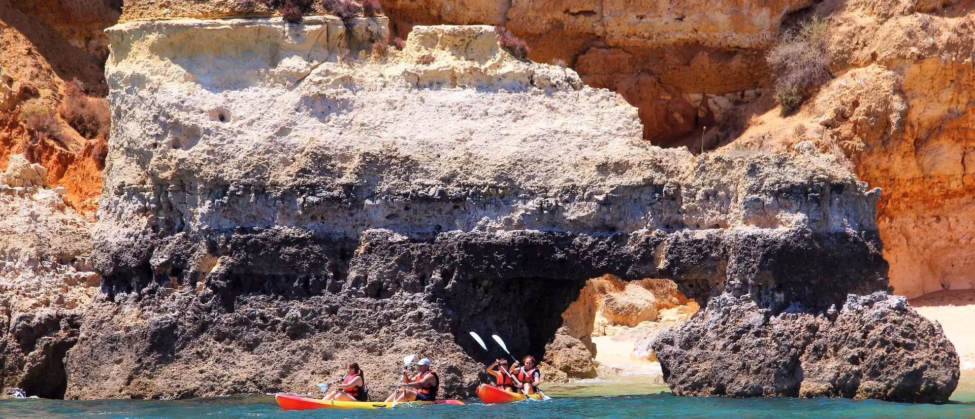 Kayakers exploring a natural rock arch and hidden sandy cove along the rugged Algarve coastline near Lagos, Portugal