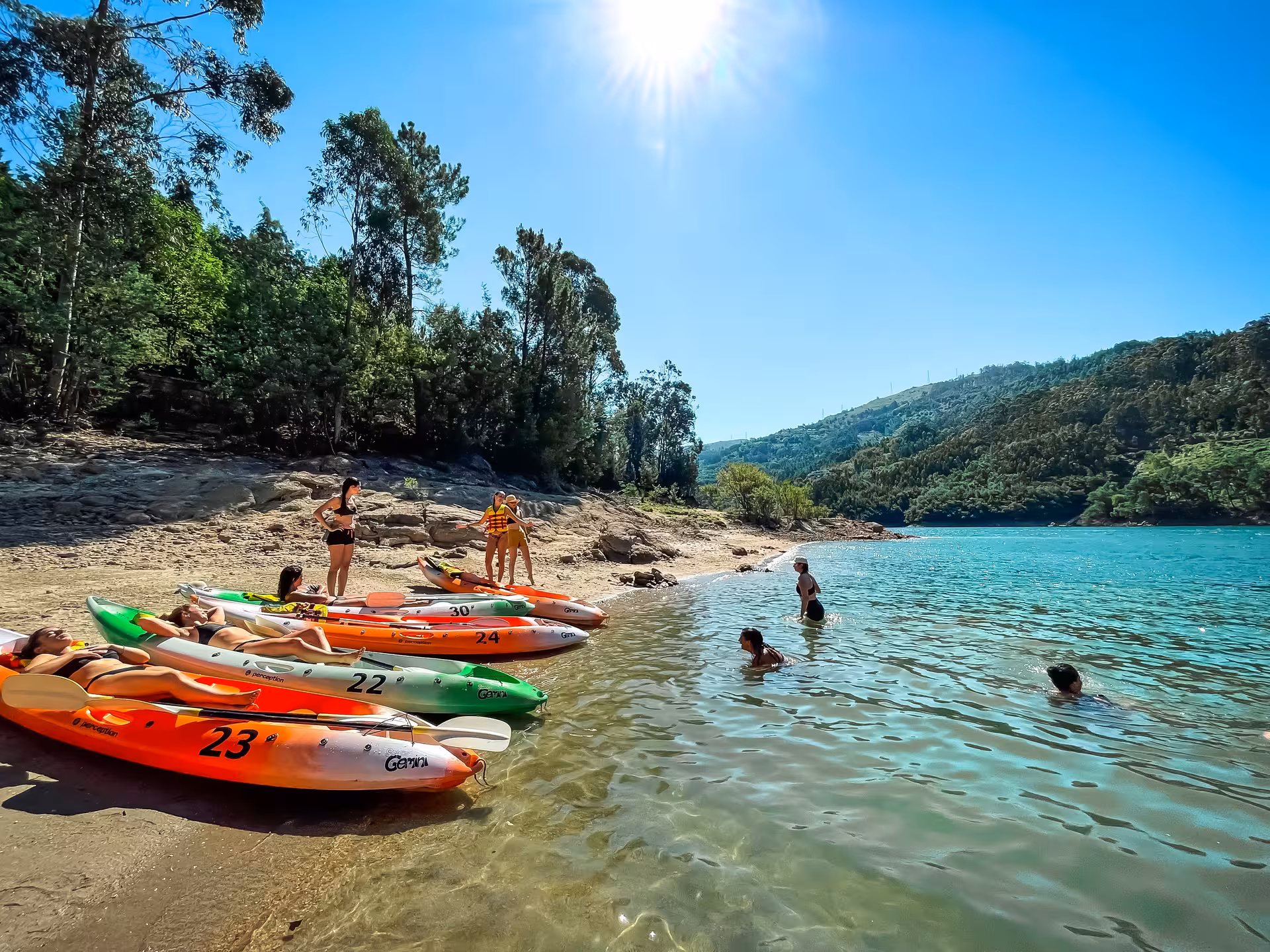 Group relaxes on sandy shore with colorful kayaks and swims in crystal-clear waters of Peneda-Gerês National Park.