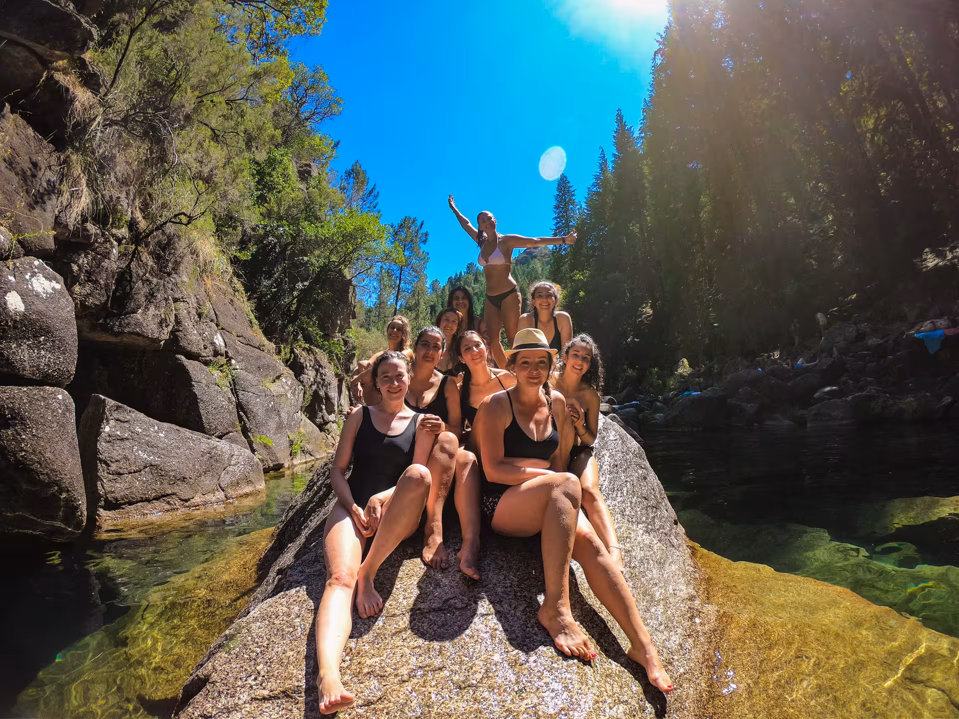 Group enjoying a sunny day on rocks by a clear river in Peneda-Gerês National Park, perfect for nature lovers.