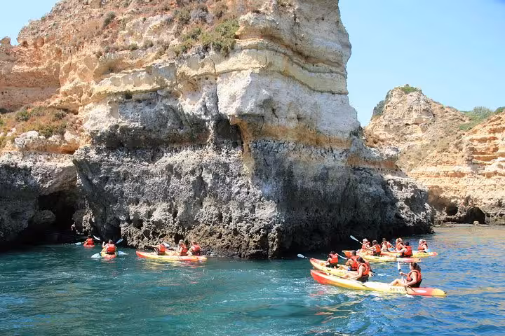 Guided kayakers in Ponta da Piedade Lagos paddling past sea cave entrance and towering Algarve cliffs