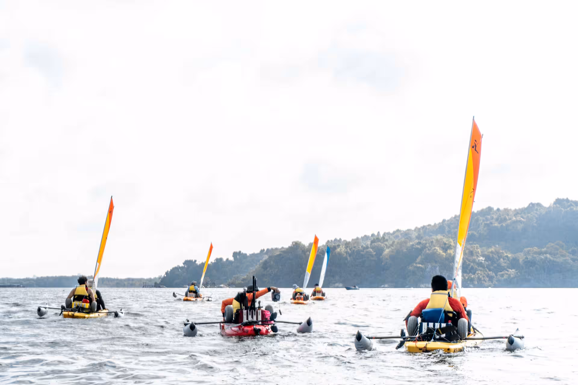 Adventurers on a thrilling kayak sailing tour, paddling towards a distant forested shoreline.