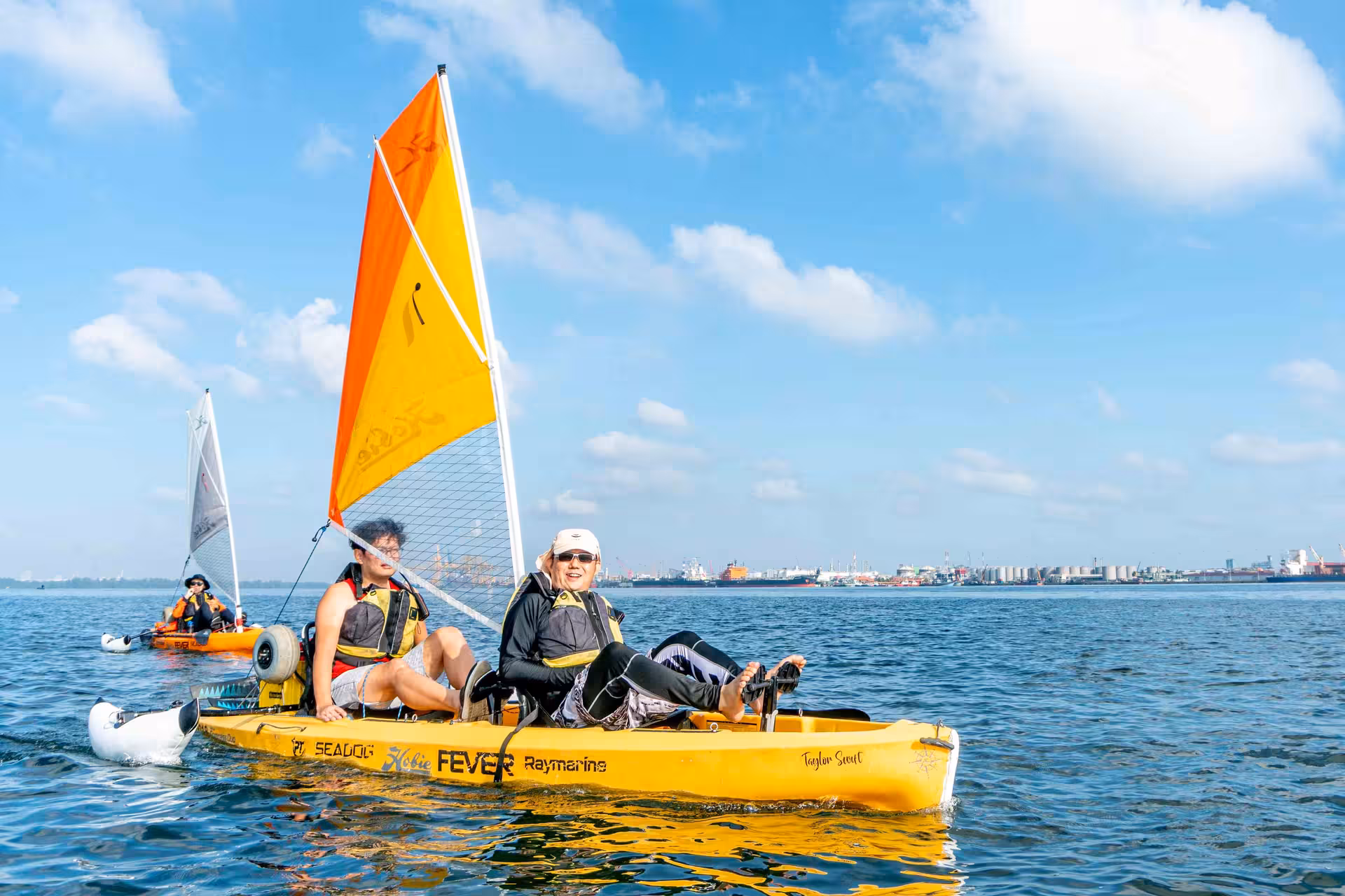 Adventurers enjoying a sunny kayak sailing tour with vibrant sails on open waters.