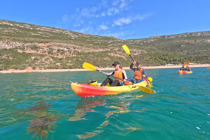 Adventurers kayaking in crystal-clear waters near Lisbon's scenic coastline, ideal for an unforgettable snorkeling and kayak tour.