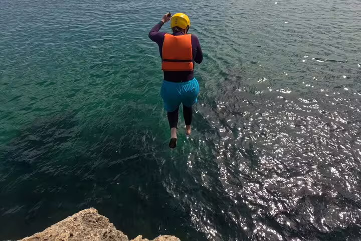 Person in a life jacket and helmet jumps into clear ocean water during a kayak and snorkeling adventure in Lisbon.