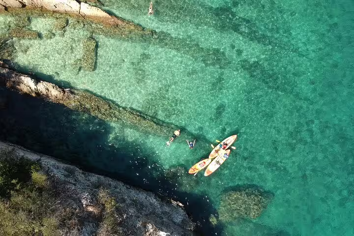 Aerial view of kayakers and snorkelers exploring crystal-clear waters along the rocky coastline near Lisbon.
