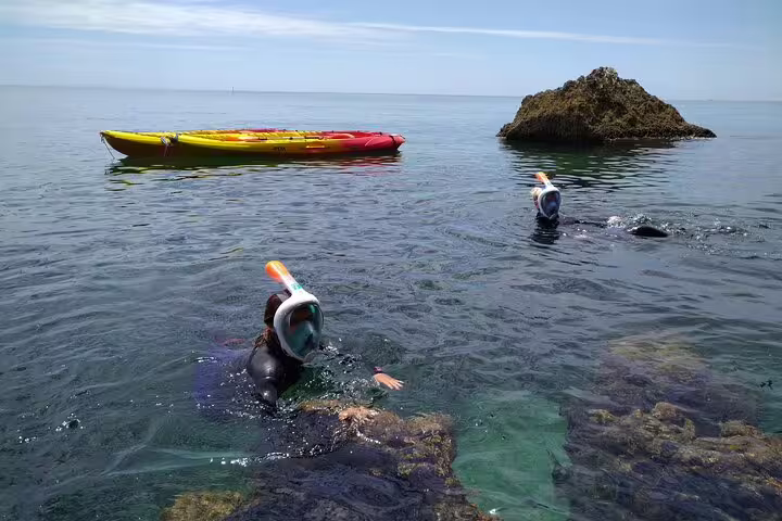 Snorkelers explore vibrant waters alongside a kayak during a Lisbon coast adventure.