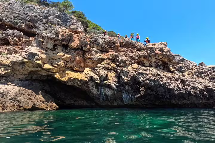 Group of adventurers exploring rocky cliffs during a kayak and snorkeling tour in Lisbon under a bright blue sky.