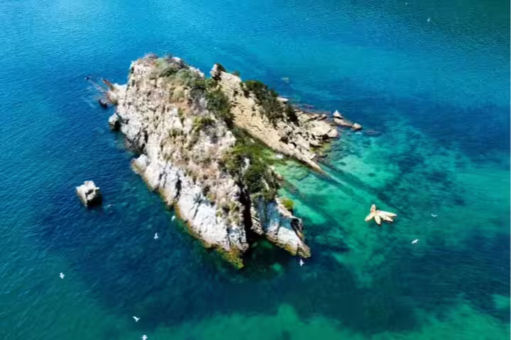 Aerial view of kayakers exploring crystal-clear waters around a scenic rocky island near Lisbon, perfect for an adventurous snorkeling tour.