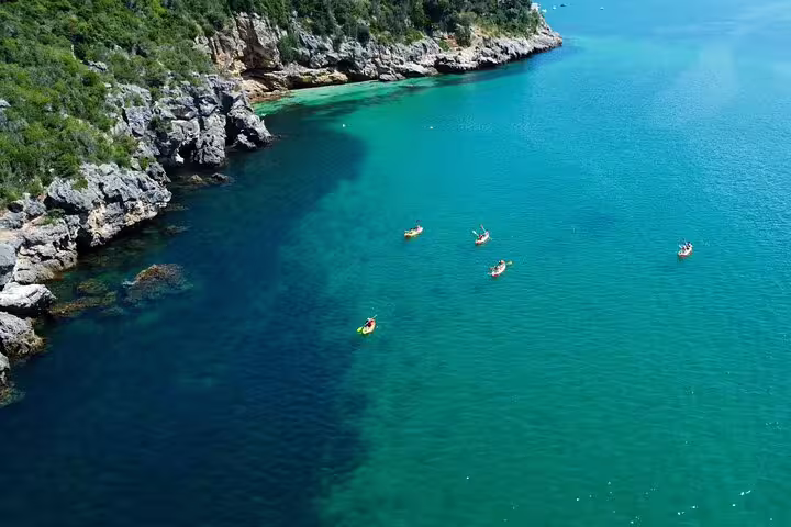 Kayakers explore the stunning turquoise waters and rocky coastline on a Lisbon snorkeling and kayaking adventure.