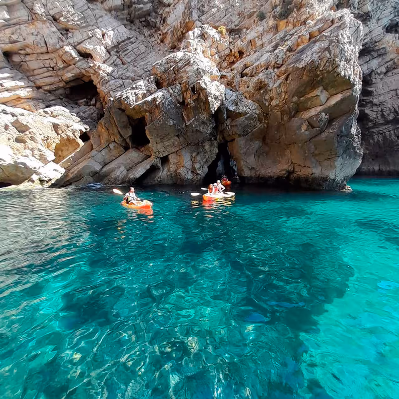 Kayakers explore vibrant turquoise waters near rocky cliffs on an adventure tour.