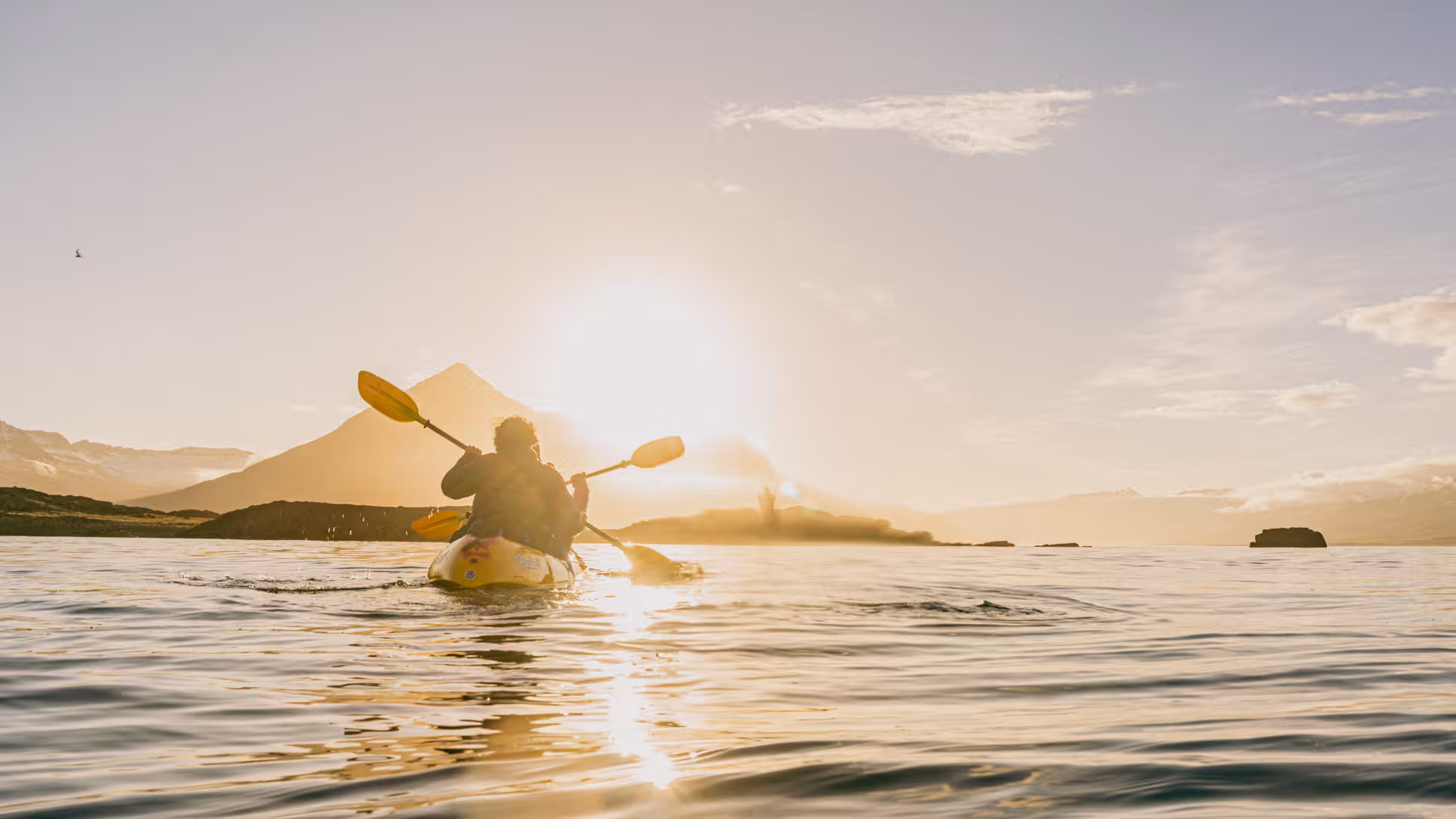 Kayaker paddles towards a stunning sunset over calm waters during a midnight kayaking tour.
