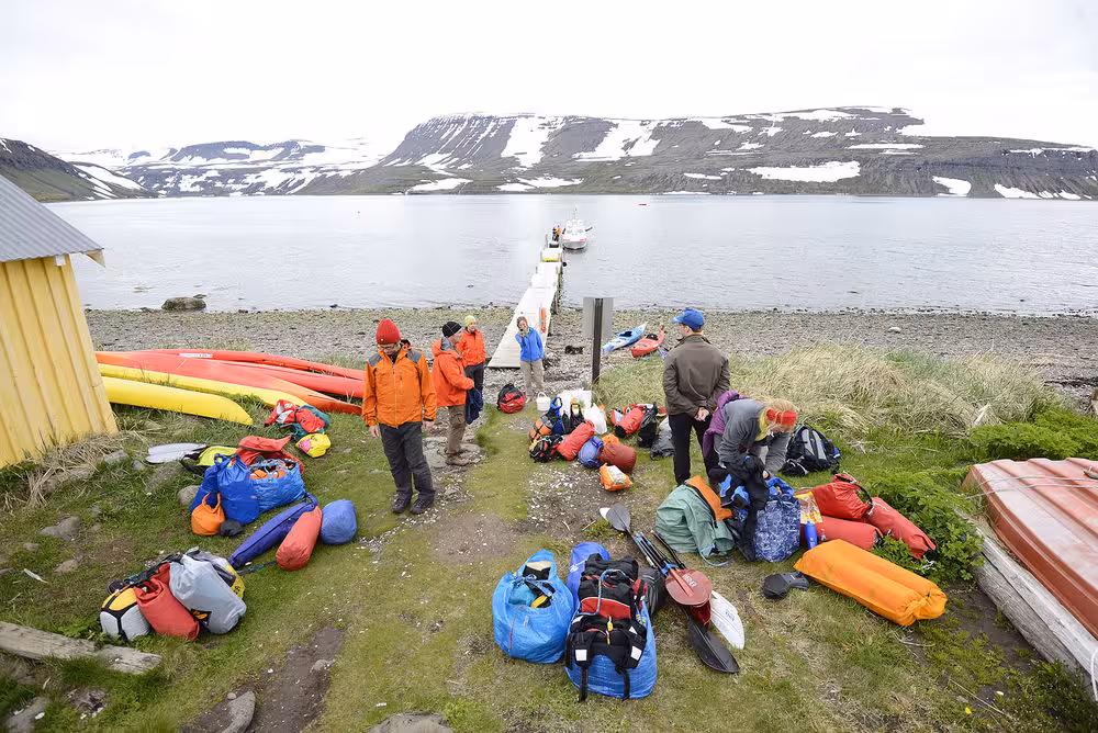 Kayakers sort dry bags and gear by a fjord pier before Paddle in the Wild sea kayaking tour in the Arctic