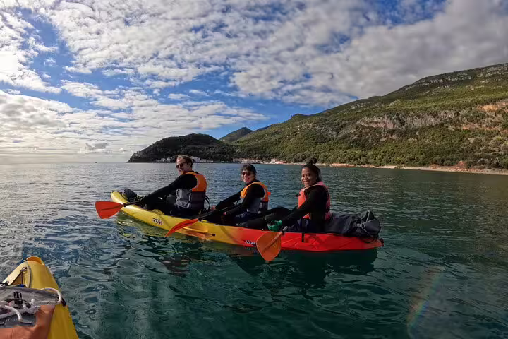 Three people enjoy kayaking in crystal-clear waters with stunning mountain views near Lisbon on a full-day adventure.