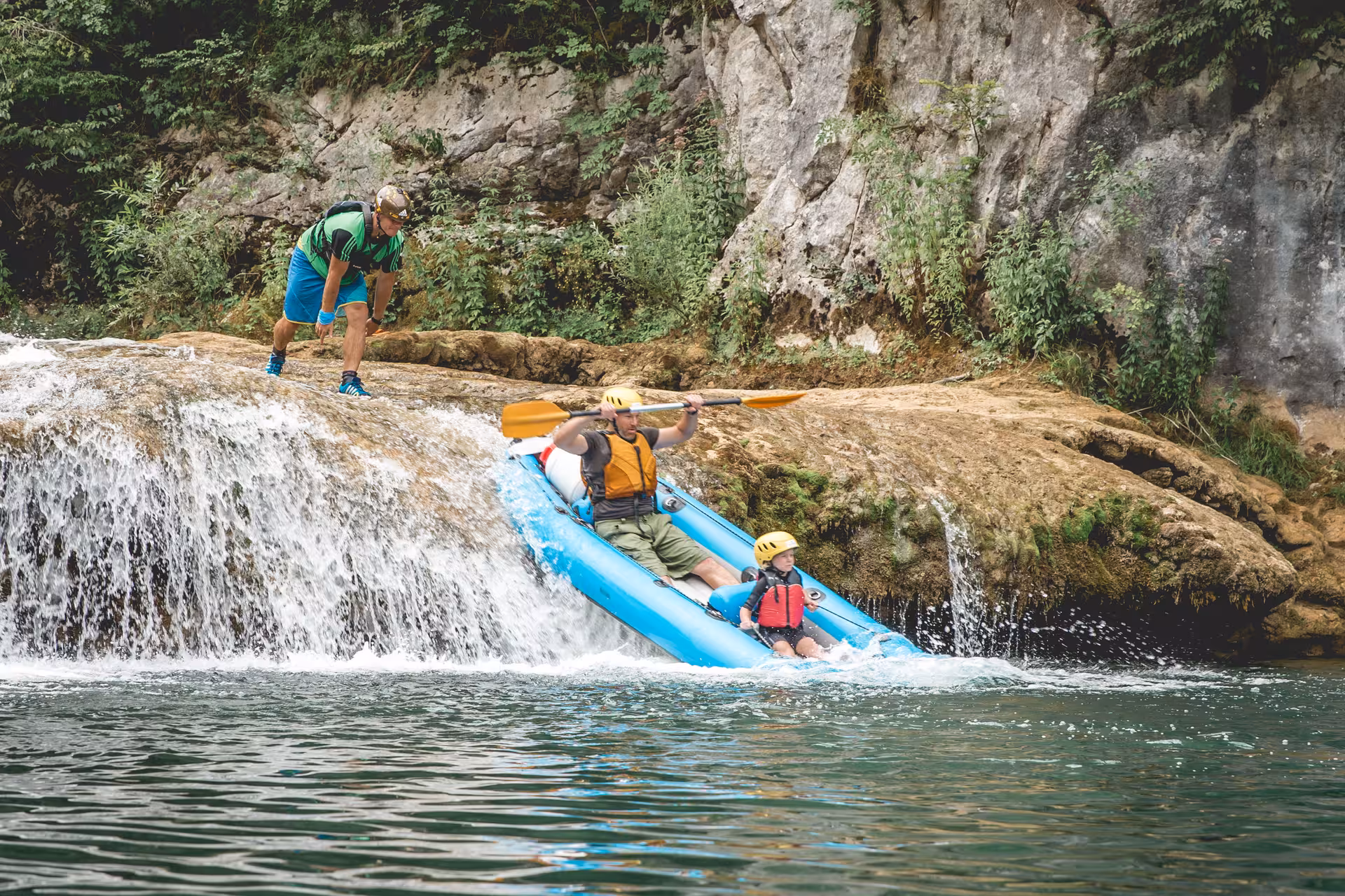 Adventurers kayaking over a small waterfall in Mreznica Canyon, Croatia, surrounded by lush greenery and rocky cliffs.