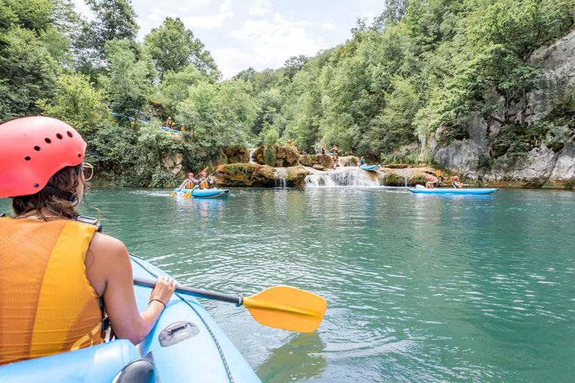 Group kayaking adventure in Mreznica Canyon with lush forests and cascading waterfalls, perfect for nature enthusiasts.