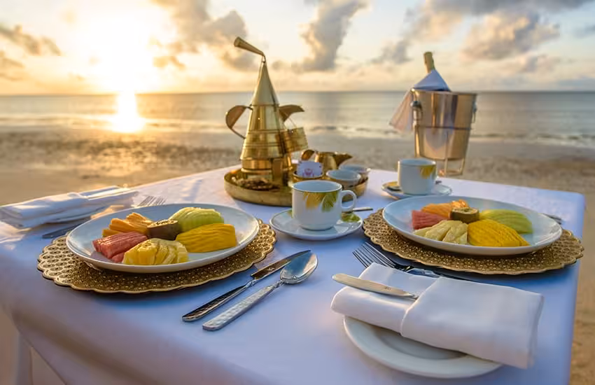 Elegant beachside breakfast setup with tropical fruits and coffee at sunrise on Kenya's coast.