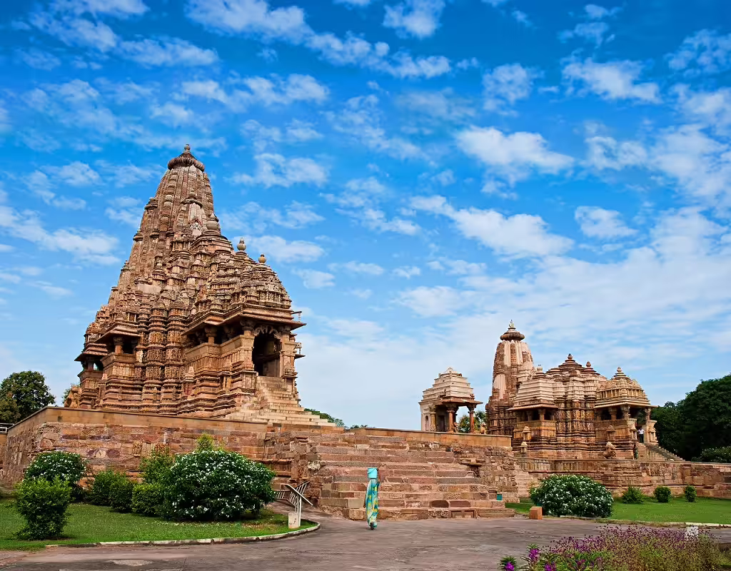 Stunning Khajuraho temples under a vibrant blue sky, showcasing intricate ancient carvings.