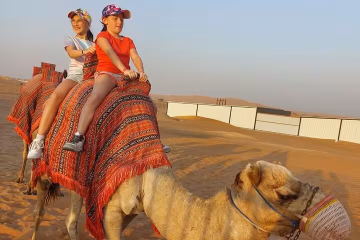 Kids riding a camel in the desert on a private morning safari, scenic dunes and traditional saddle blanket