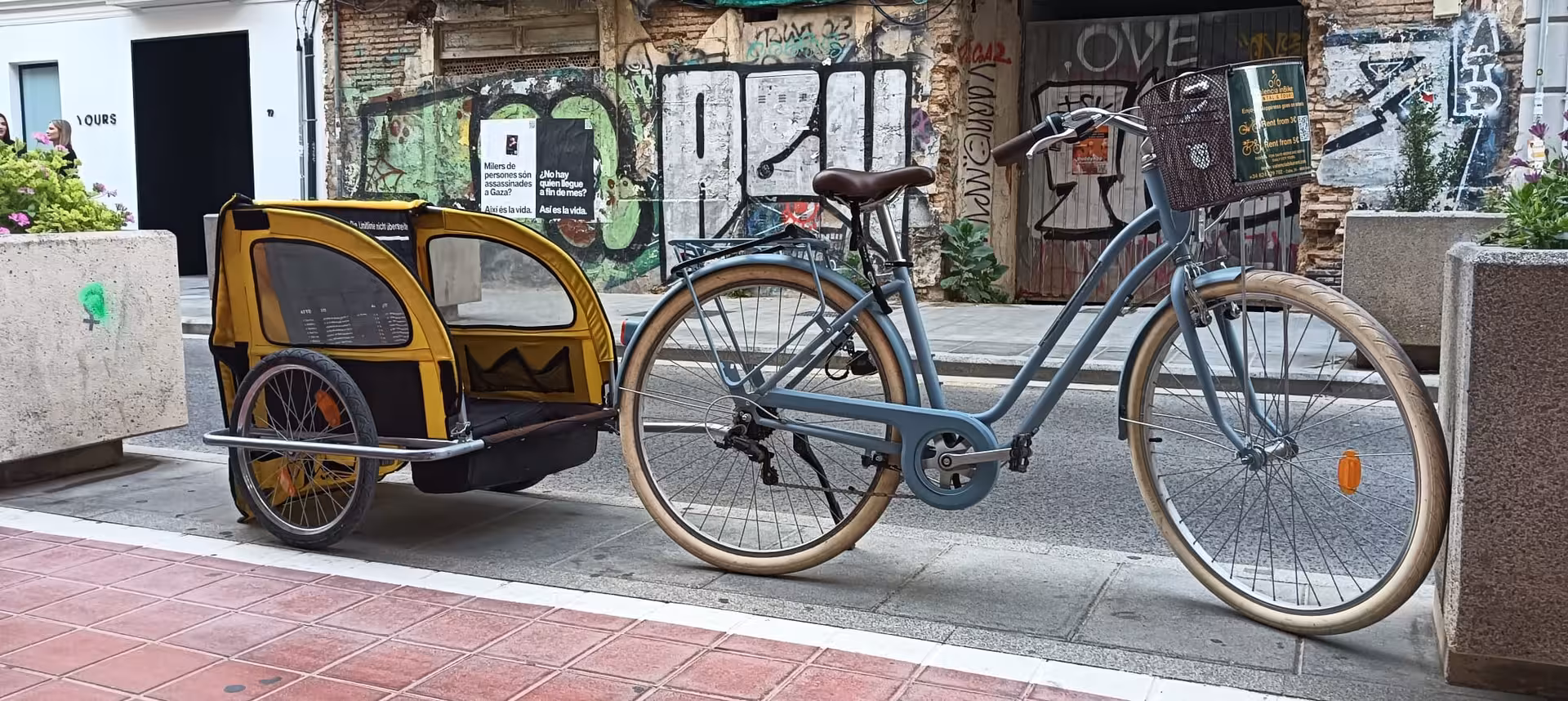 Family city bike rental with child trailer parked by street art wall, safe kids cycling option in town