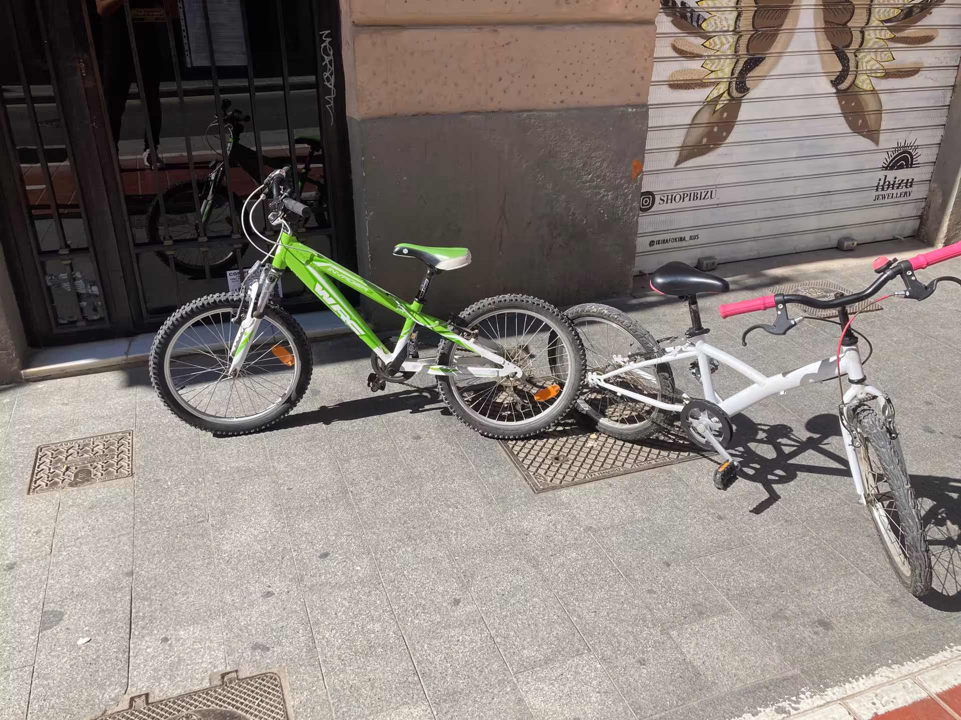 Two kids city rental bikes on sidewalk, green and white frames, ready for family cycling in town