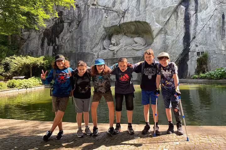 Kids group photo by the Lion Monument and pond in Lucerne, enjoying a self-guided scavenger hunt walking tour