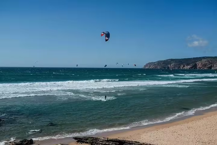 Kitesurfers enjoy the waves at a sunny Guincho beach, captured during a private Sintra, Cabo da Roca, Cascais tour.