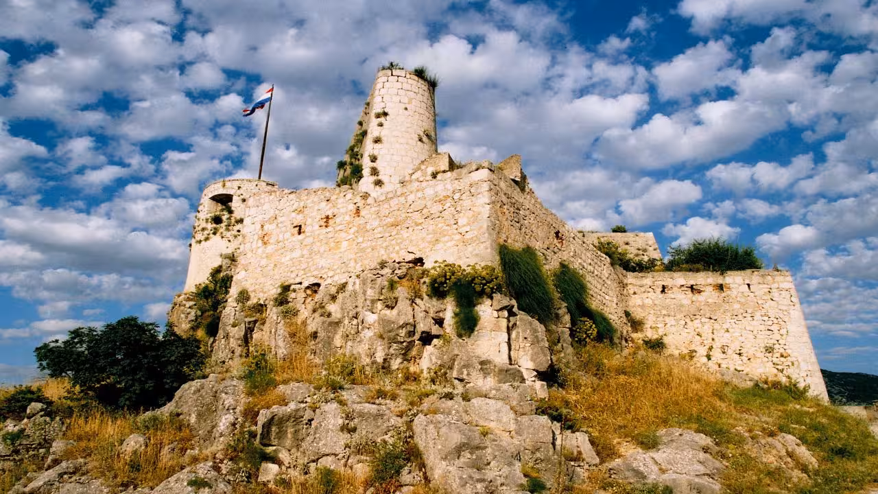 Klis Fortress above Split, Croatia, stone walls on rocky hill with flag, panoramic views tour stop