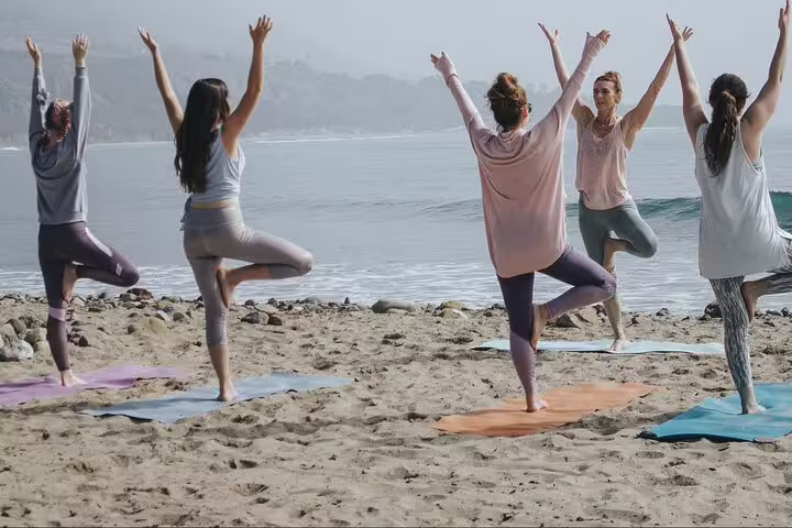 Group practicing yoga on a serene Kos beach at sunrise, enhancing wellness amidst calming sea views.
