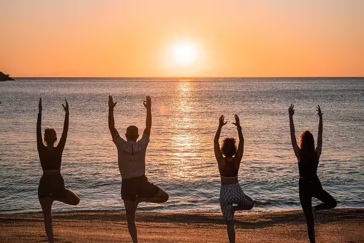 Four people in yoga poses by the sea during a stunning Kos sunrise.