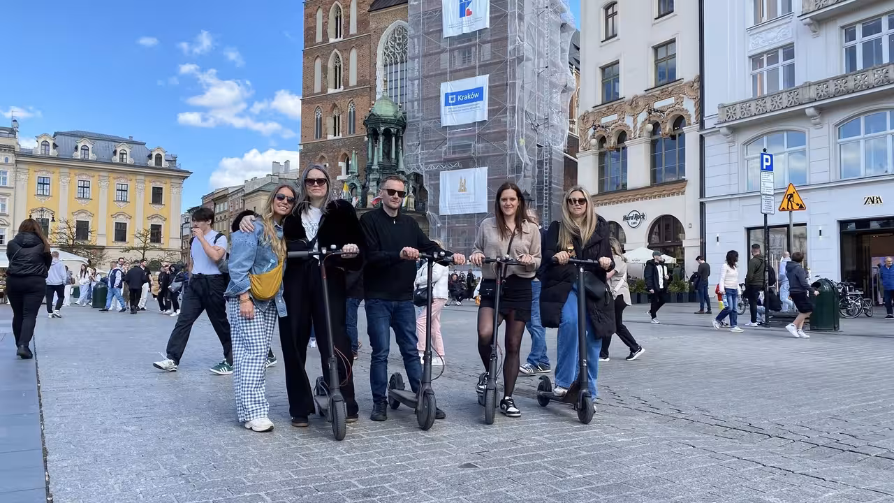 Group enjoying e-scooter rentals in Krakow's historic square under a clear blue sky, perfect for sightseeing adventures.