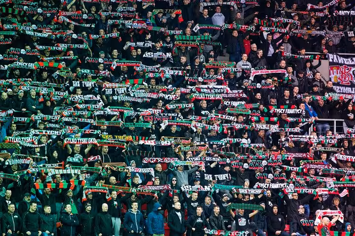 Krakow football match with local host, packed ultras stand waving scarves and chanting in the stadium