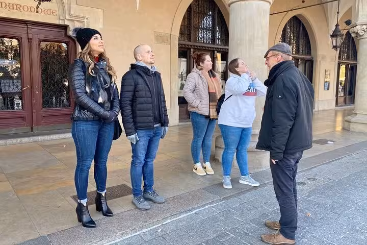 Tour guide leading a group in Krakow's Jewish Quarter, highlighting historic architecture on a sunny day.