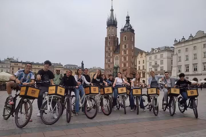 Tourists on a bike tour in Krakow's Old Town, posing in front of iconic St. Mary's Basilica for a memorable experience.