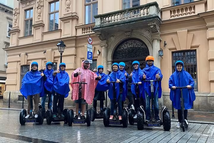 Group on Krakow private Segway tour in blue ponchos, exploring historic architecture on a rainy day.