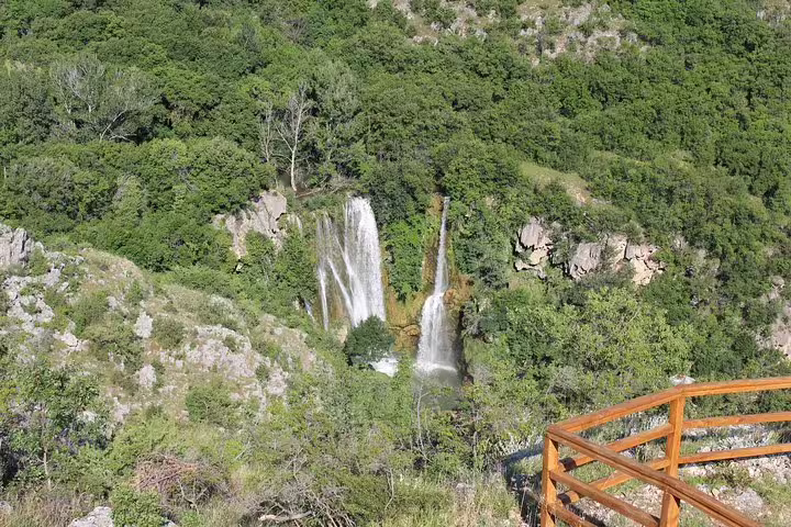 Viewpoint over cascading Krka National Park waterfalls framed by lush forest and wooden railing lookout