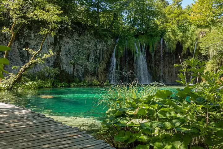 Waterfall spilling into emerald lake beside wooden boardwalk at Plitvice Lakes National Park tour from Split