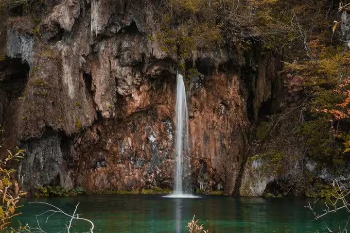 Tall Plitvice Lakes waterfall dropping into calm green pool, scenic stop on guided group tour from Split