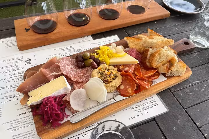 Delicious charcuterie board with assorted cheeses, meats, and bread paired with wine on the Kumeu Wine Tour.