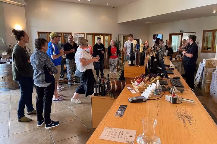 Group being introduced to a variety of wines at Kumeu Wine Tour, with bottles displayed on the counter.
