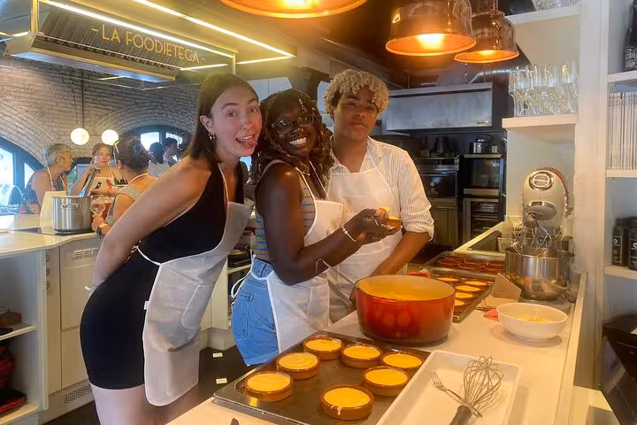 Three participants smiling while preparing gourmet desserts in a premium cooking class at La Boqueria Market tour.