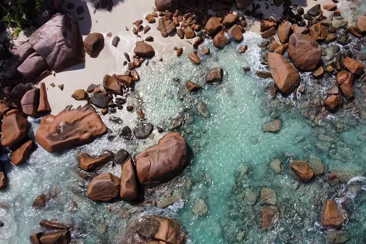 Aerial view of turquoise waters and granite boulders on La Digue, highlighting the island's natural beauty on a day trip.