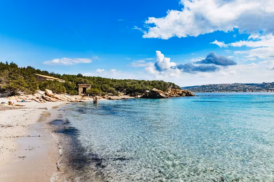 Pristine sandy beach and clear blue waters of La Maddalena Archipelago under a bright, sunny sky.